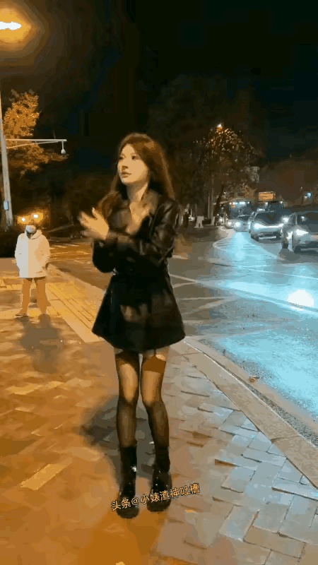 女子穿着打扮很时髦，上穿黑风衣，下穿丝袜短裤，就是不知道她这么穿冷不冷？她身后有