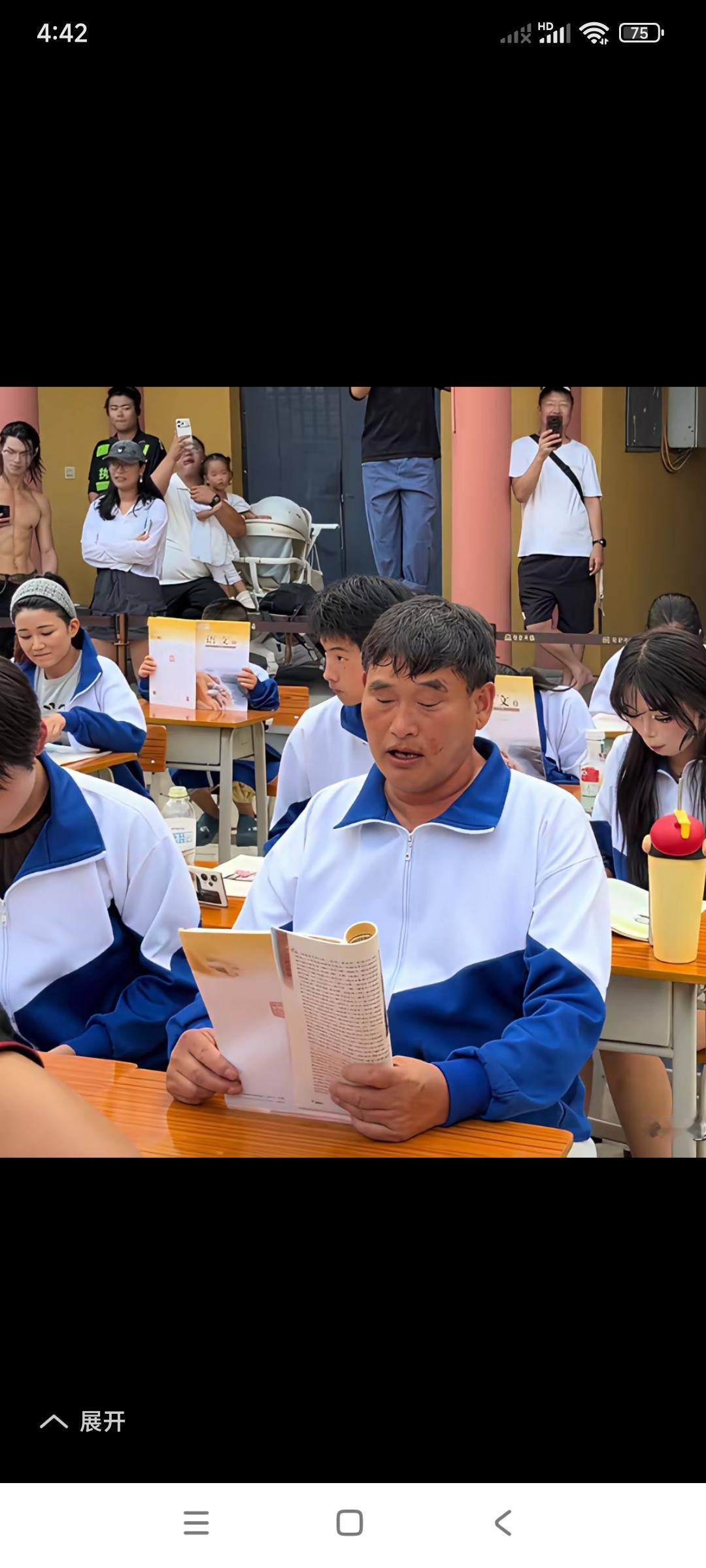 拿起书本儿装模作样的，坐在众多小学生中间。

大衣哥朱之文穿上了学生的服装，坐在