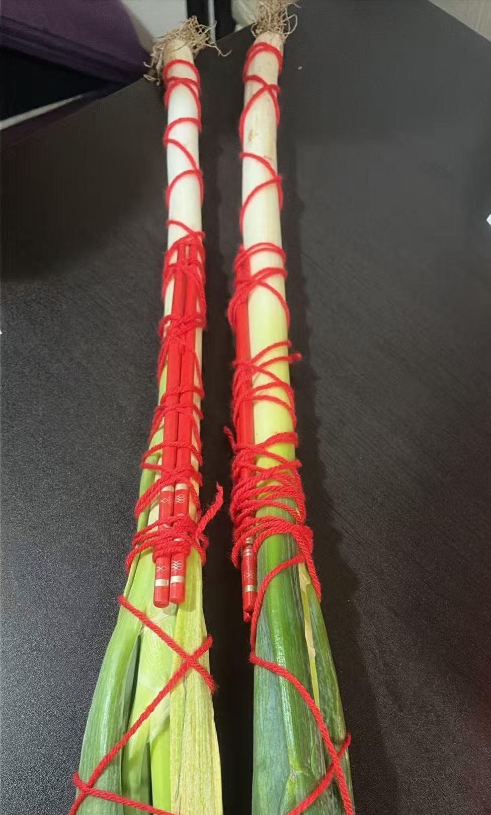 今天新婚儿媳妇收拾娘家带来的东西，发了照片给我，两根葱上用红绳各绑着两根红筷子。