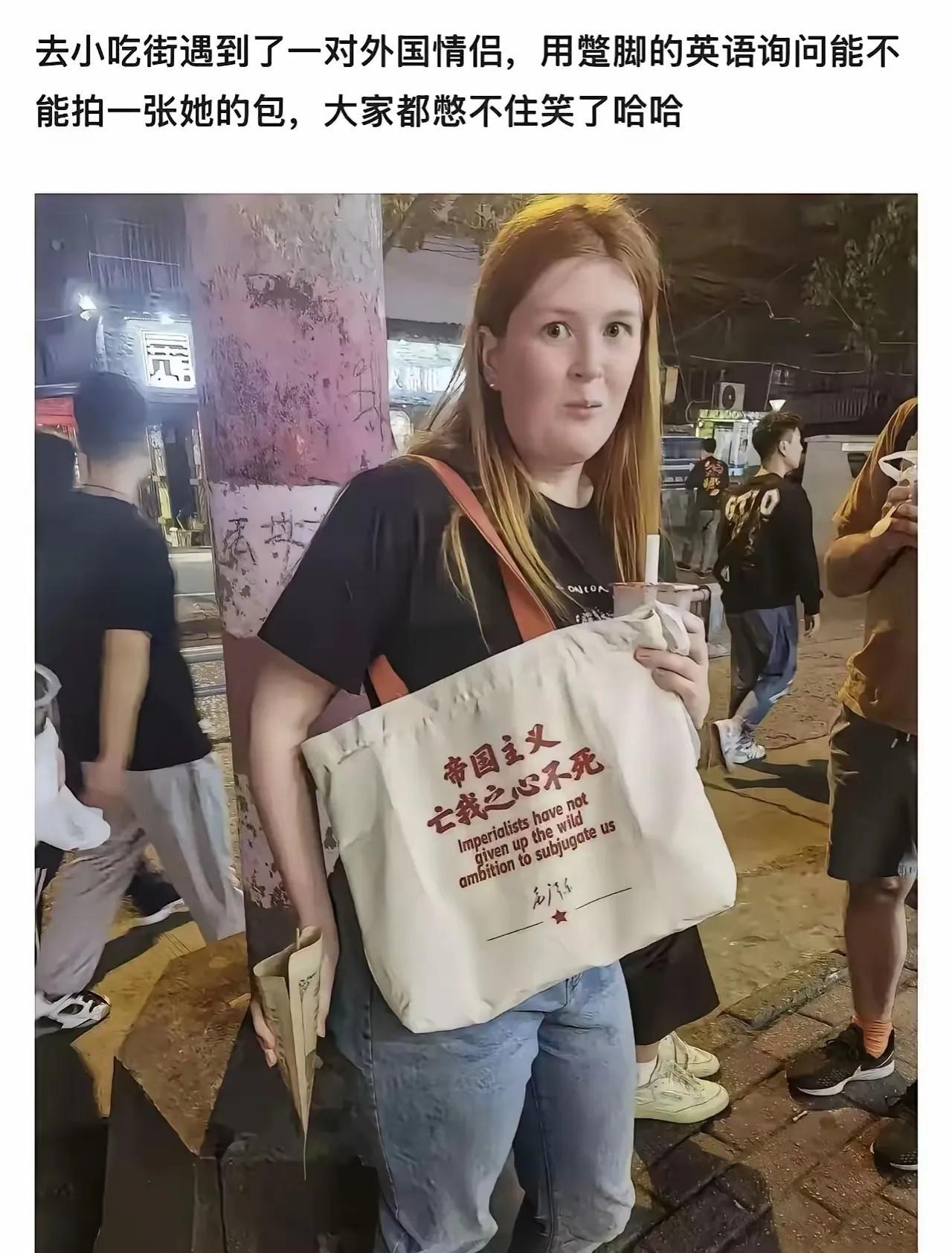 这个洋妞也反对帝国主义！在一个小吃街上，一个洋妞背着一个帆布包，包包上印着“帝国