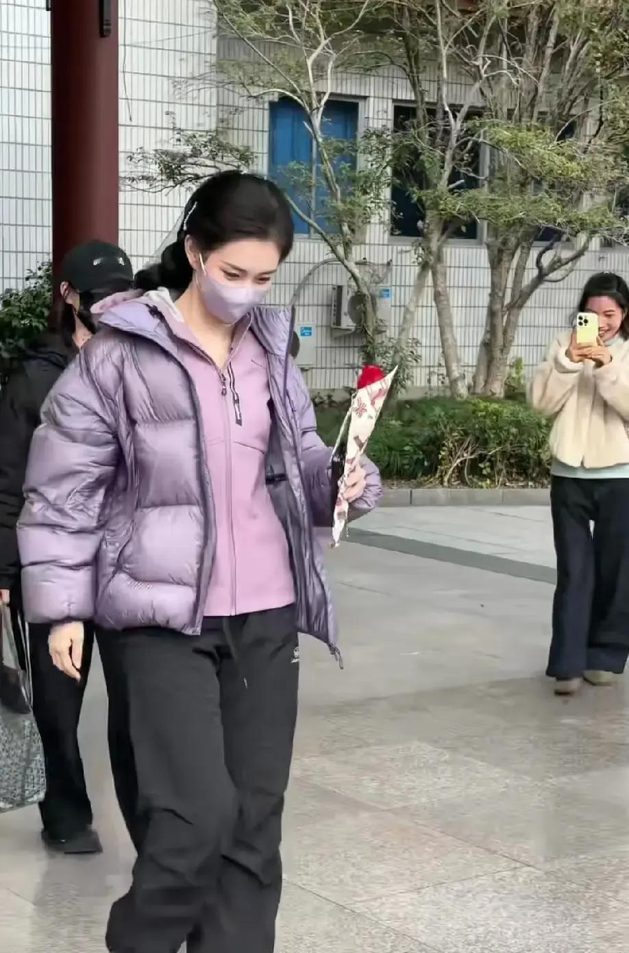 别信什么“大红大紫”的玄学。
横店这位穿紫衣拿玫瑰的千金，靠的不是道具，是一套被