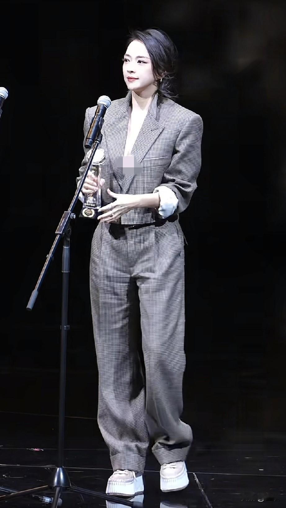 在澳门电影节的舞台上，章子怡身着格纹西装套装。她手捧奖杯，在聚光灯下闪耀，四封影