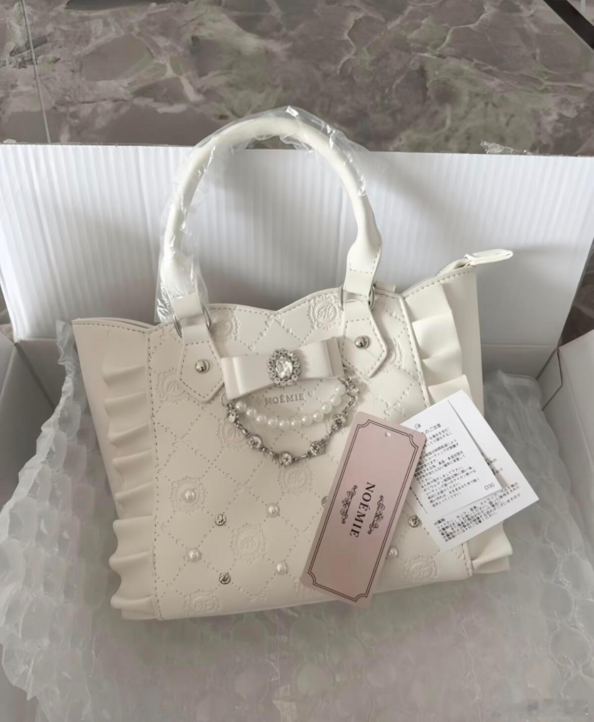 这款“NOEMIE”品牌的手提包是一件极具洛丽塔风情的精致饰品。纯净象牙白色包身