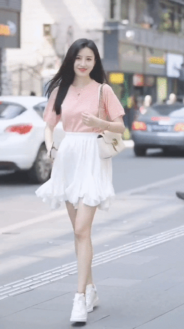 穿粉色上衣和白色裙子的女孩在街上走。笑容满面，