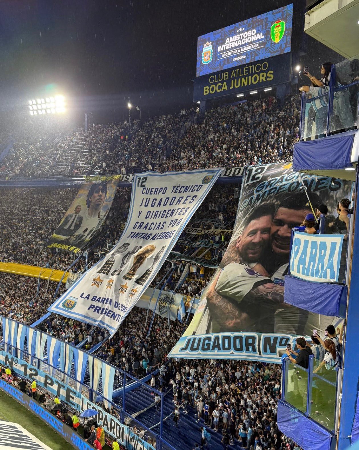 糖果盒球场的球迷们升起横幅，向梅西和帕雷德斯致敬，上面写着“谢谢你们，冠军们！”