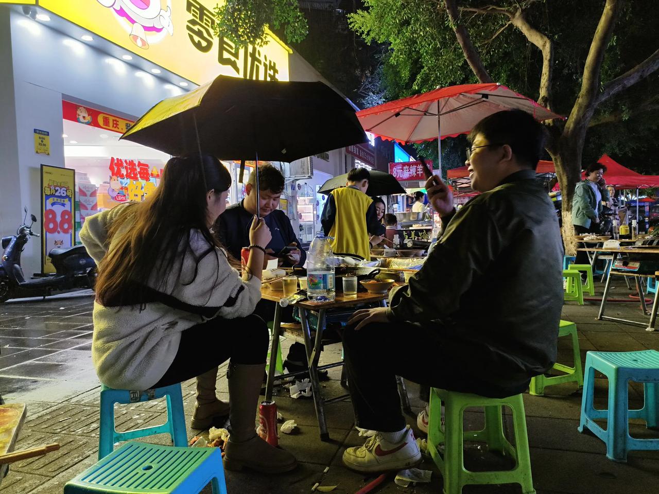 2024年10月11日晚，在重庆回兴的地摊火锅旁，一位优雅的女士手持雨伞，悠然自