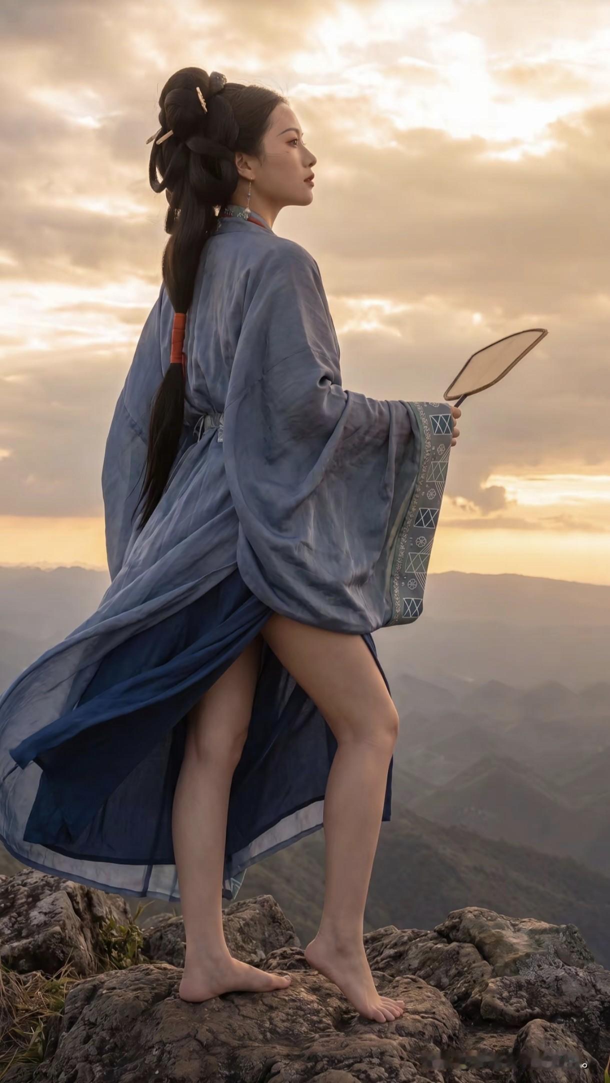 一袭深蓝汉服，立于群山之巅，
像是从武侠世界里走出的隐世侠客。
身畔是连绵起伏的
