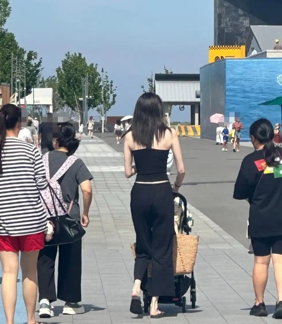 何穗带着孩子去阿那亚游玩，无修照片里皮肤白皙细腻，儿子坐在推车中悠闲地翘着小腿好