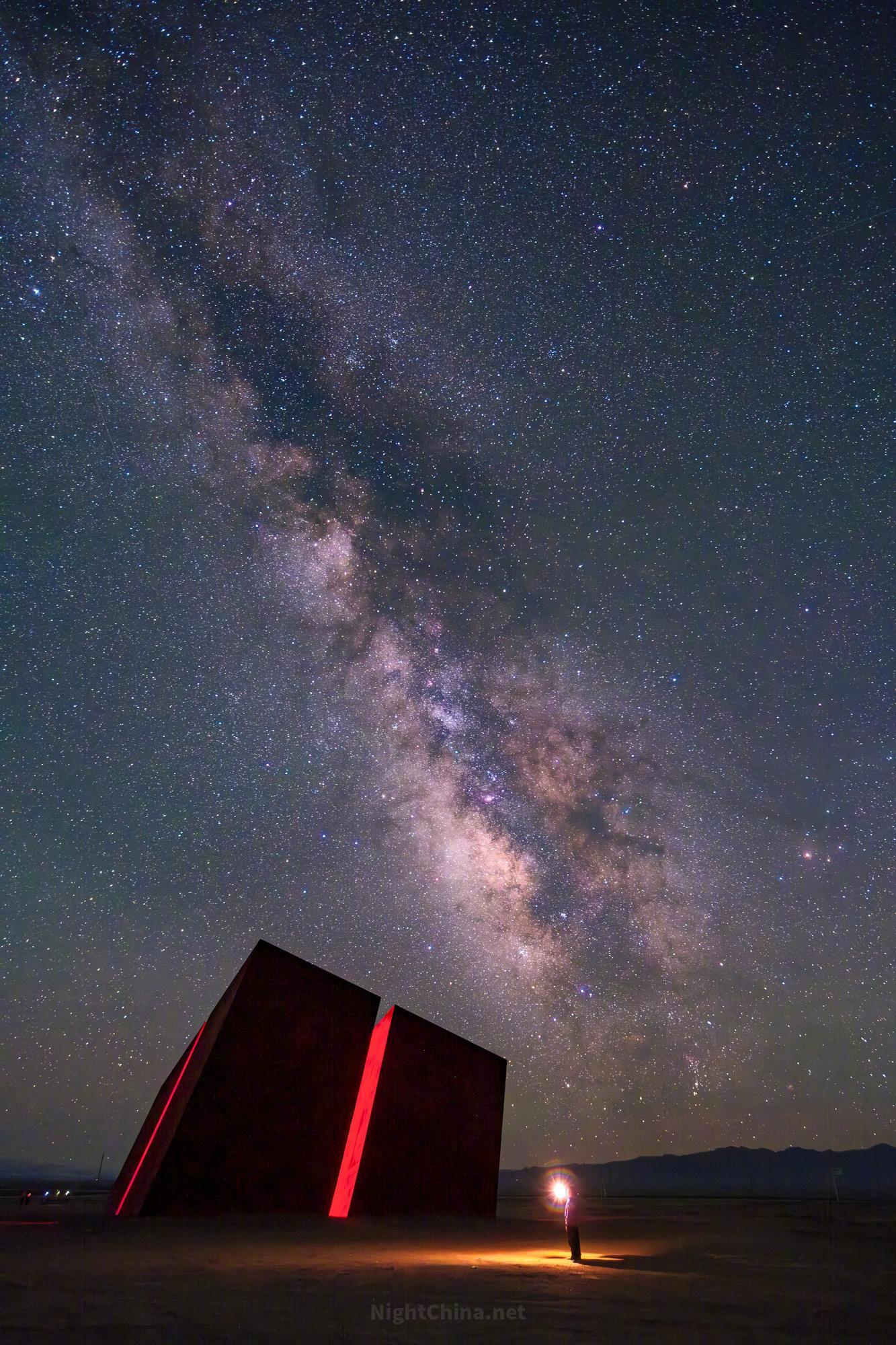 银河自天顶倾落，正好压在那道红墙的上方，像是宇宙选了这里作为入口。一盏孤灯，在旷