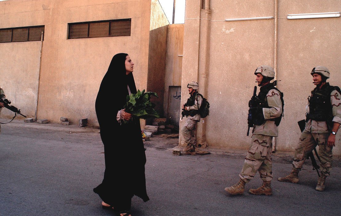 2003，伊拉克，巴格达，一位女子和美军士兵们擦肩而过 
