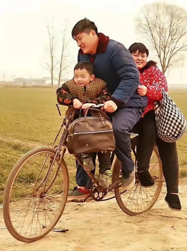一辆略显陈旧的二八大杠，一个黑色皮包挂在车把上，前面大梁上坐的是孩子，后面车座子