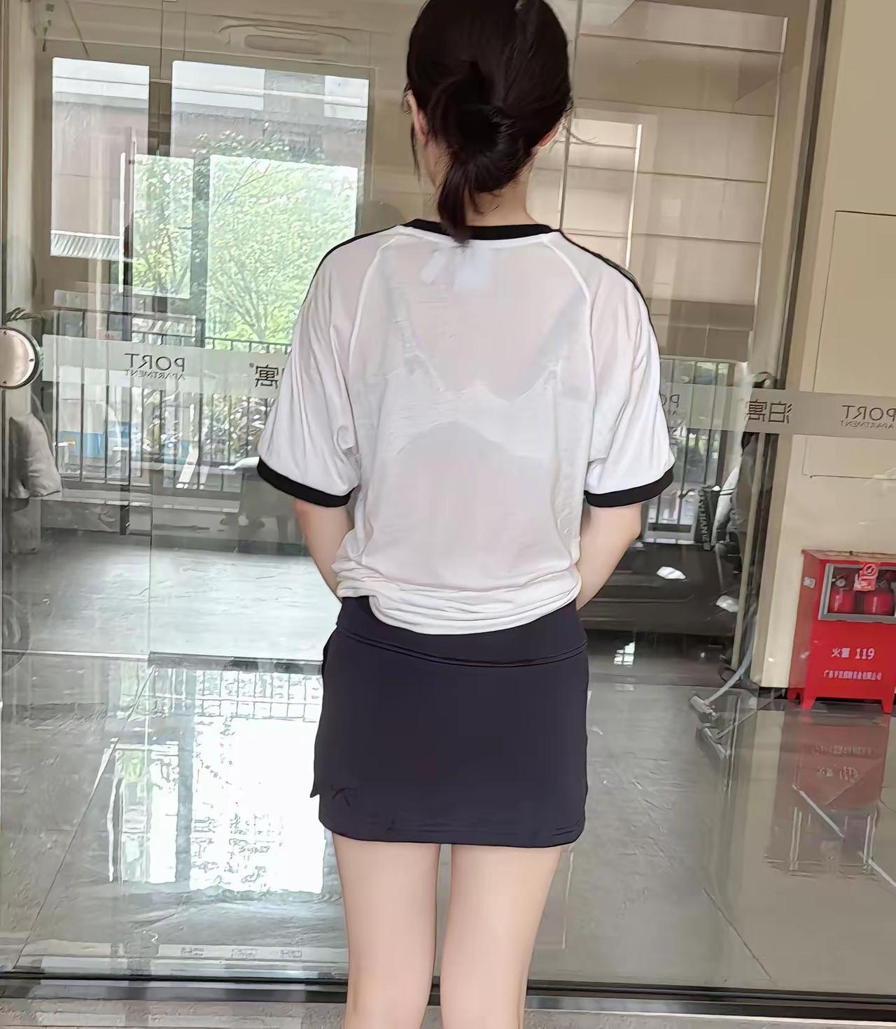 她的背影透着随性的运动感，乌黑的头发束成低马尾，白色短袖上衣后背被汗水浸湿，布料