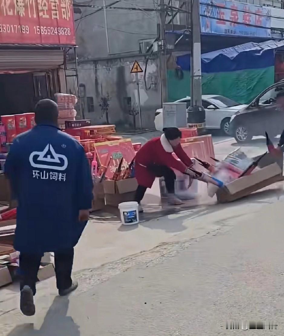 又一家鞭炮小卖部着火了，男的反应迅速把箱子拉马路中间去了，这女的还在那往回扒拉