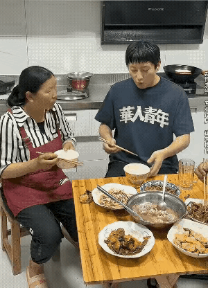 一家三口在吃饭，儿子吃完了一碗饭，用筷子指着碗对妈妈说，我的饭吃完了，赶快给我盛