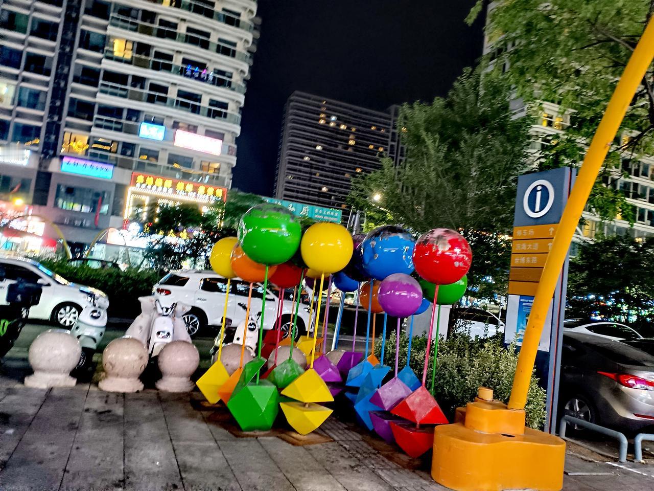 夜色楼宇灯火璀璨，彩色气球雕塑立于街边，鲜活装点都市晚风。