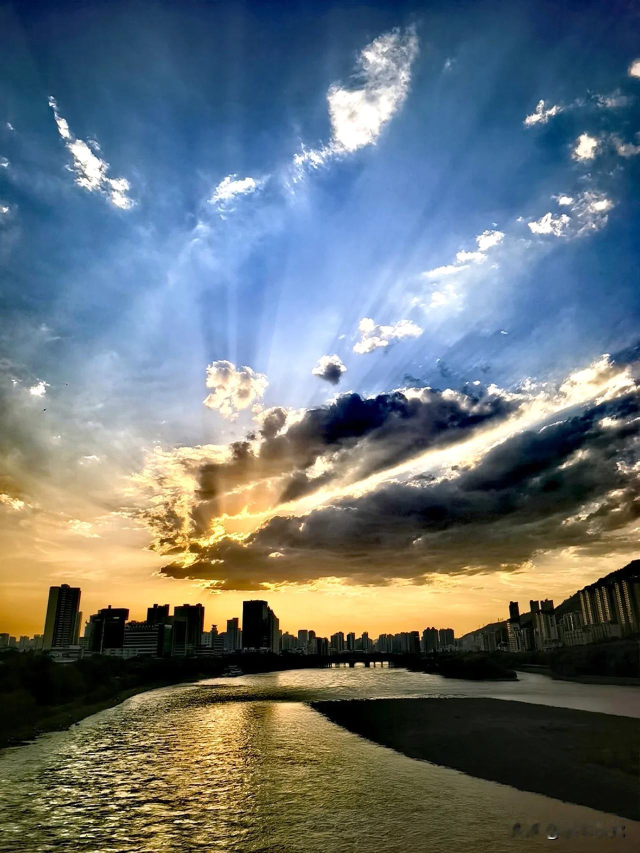 今日醉晚霞:落日穿破层叠云幔，万丈丁达尔光束倾泻长空，半边天际染成温润橙金，远天