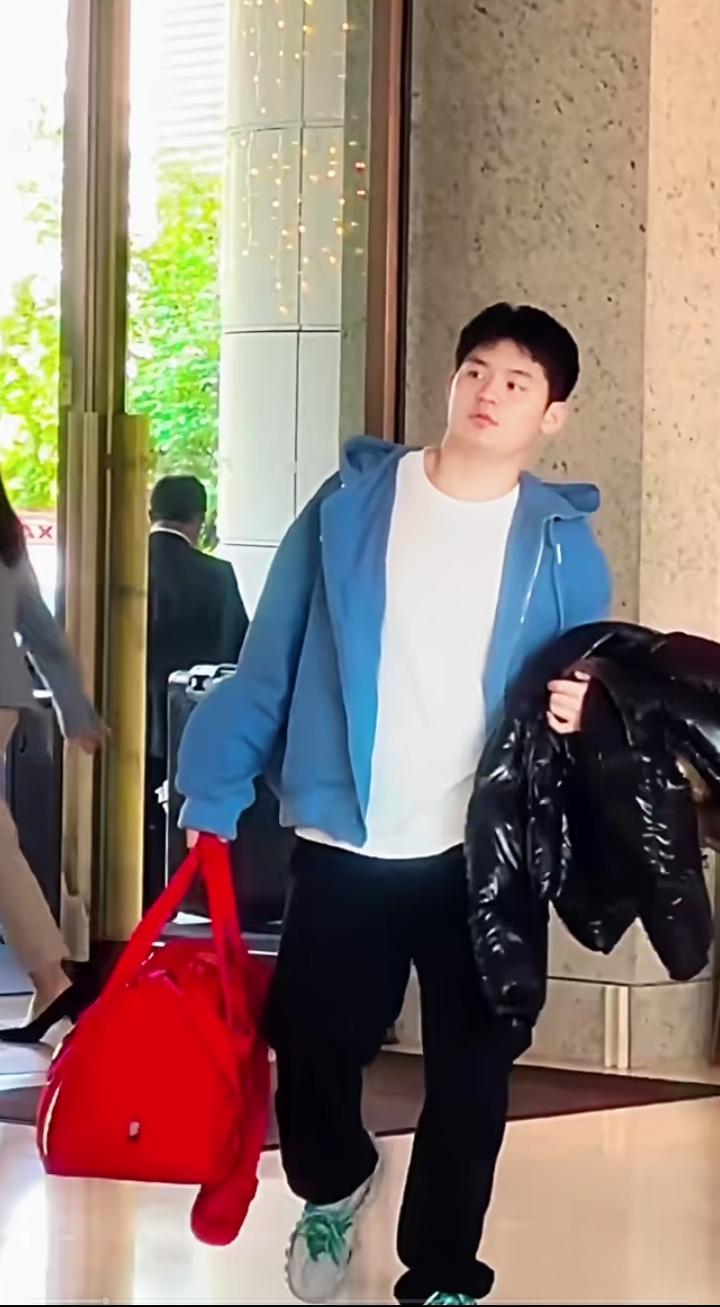 林诗栋太青春活力满满！只见他一手拿着红色行李包，一手拿着黑色羽绒服，那模样随性洒