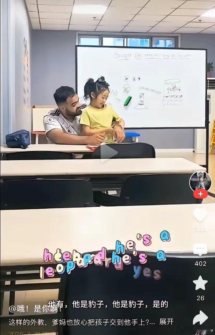 这张短视频截图拍摄于少儿英语培训机构的教室内，画面里外籍男外教将年幼的小女孩搂抱