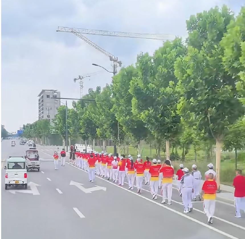 6月10日，河南商丘，一支统一着装的徒步队伍，在城市道路非机动车道上集体行进，挤