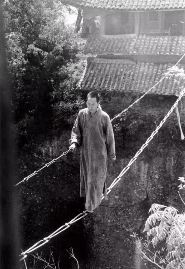 1930年代，在四川江油窦圖山上的寺庙里，一位出家人正踩着一根简陋的铁链子过悬崖