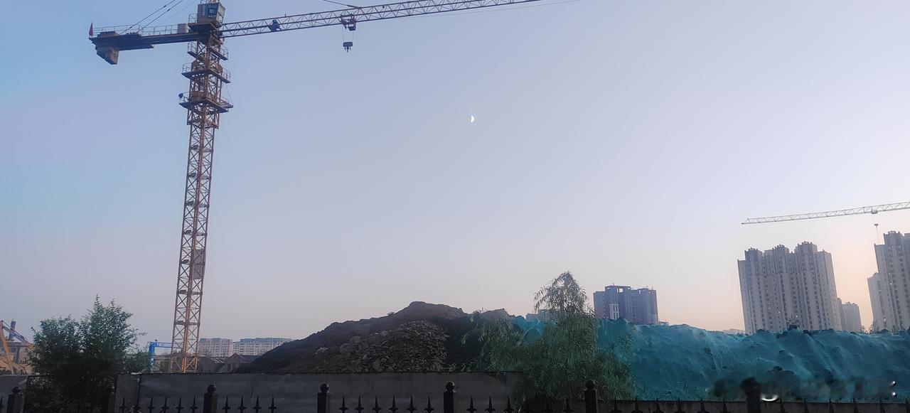 天色刚擦上暮色，弯月早早挂在淡青色天空，工地塔吊静静立在一旁。堆起的土坡盖着绿网