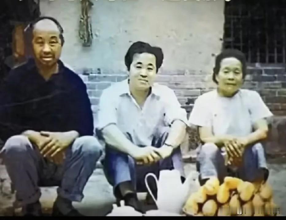年轻时的莫言在老家山东高密与父母坐在自己院墙根的一张留影，面前还有一筐刚收下来的