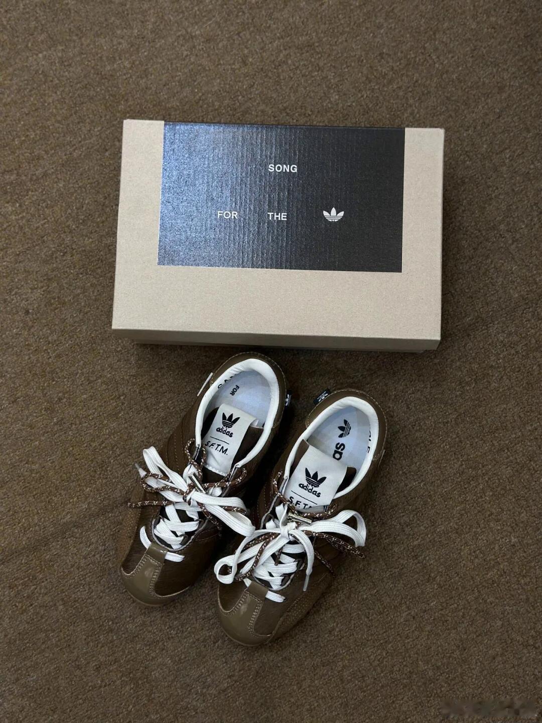 这双阿迪达斯运动鞋以深棕色麂皮鞋面尽显复古质感，标志性的白色三条纹与侧身三叶草L