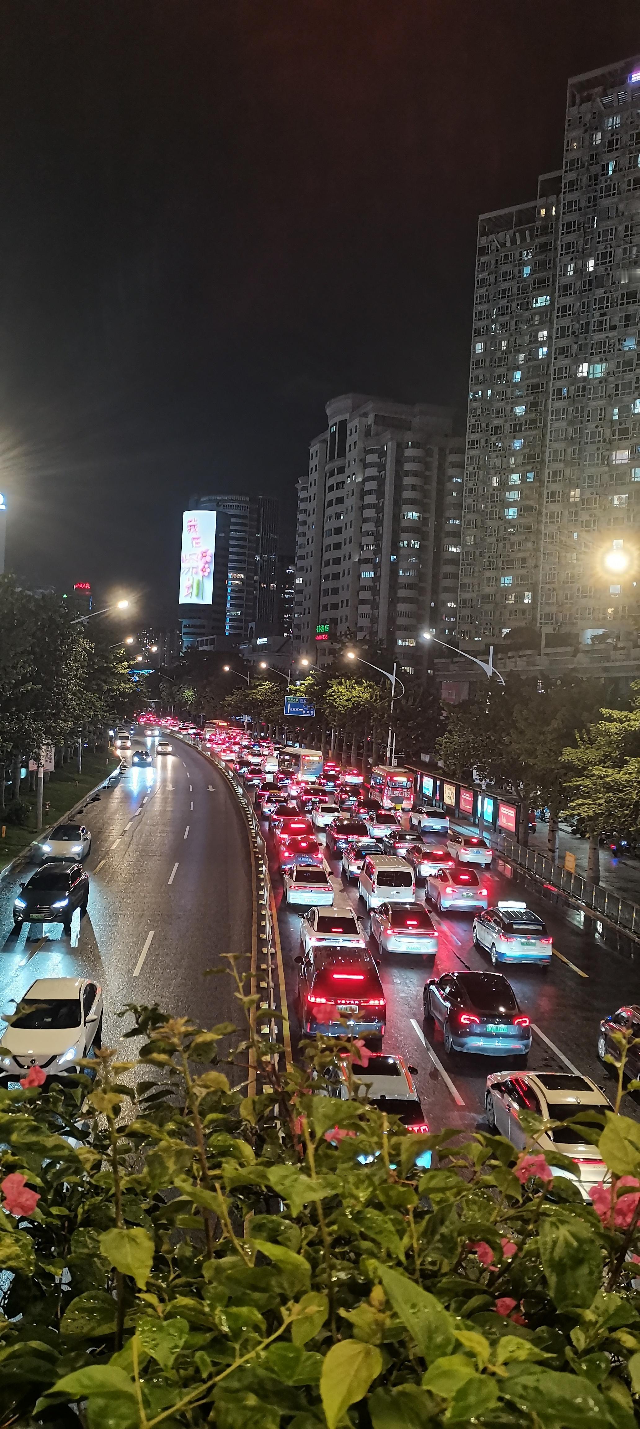 一场夜雨刚落下，路面泛着湿润透亮的水光。夜幕笼罩城市，高楼灯火次第亮起。长长的车