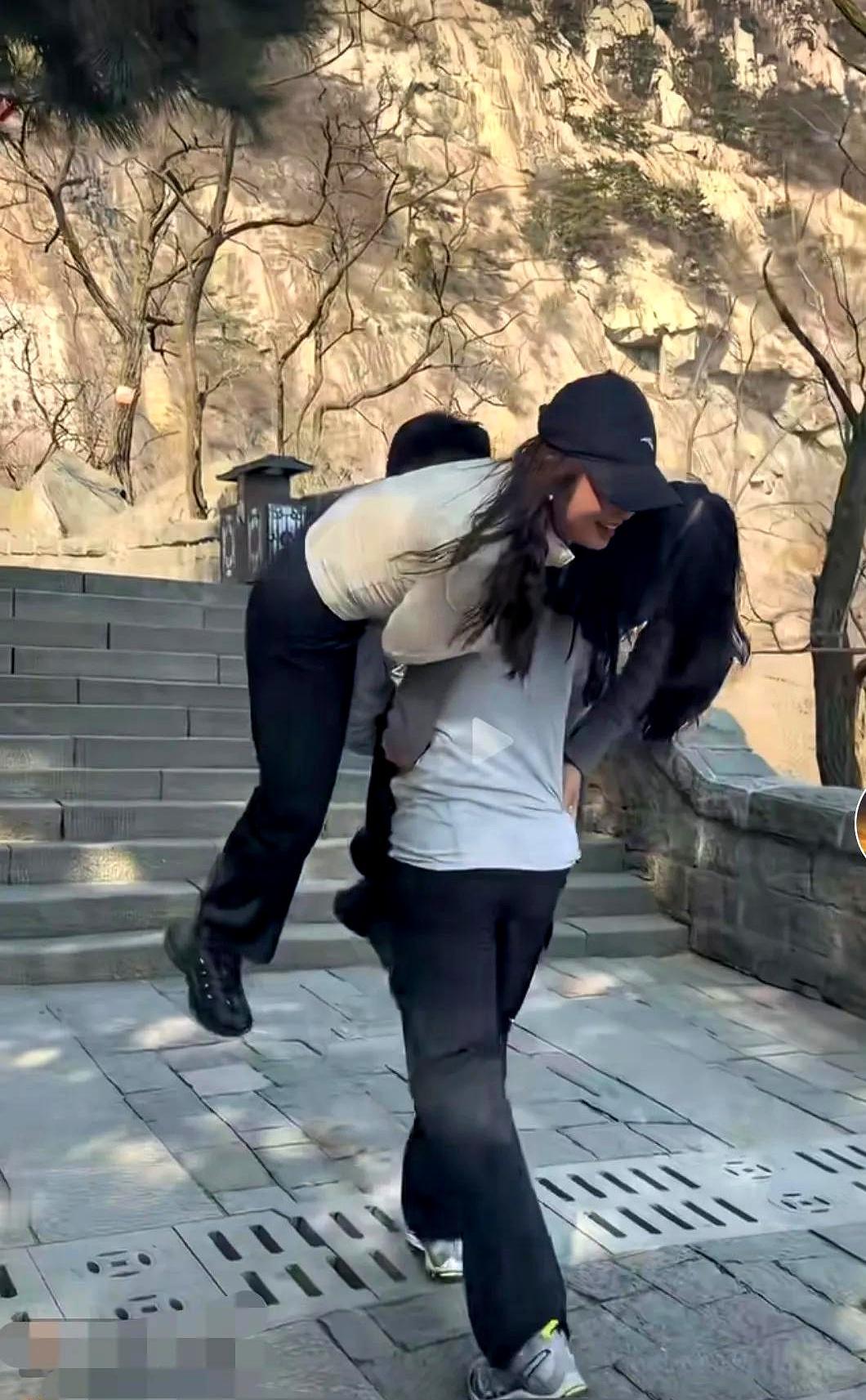 视频里，泰山石阶上，一个年轻人弓着背，左右各一位游客坐在绑带上，像挑担子一样往上