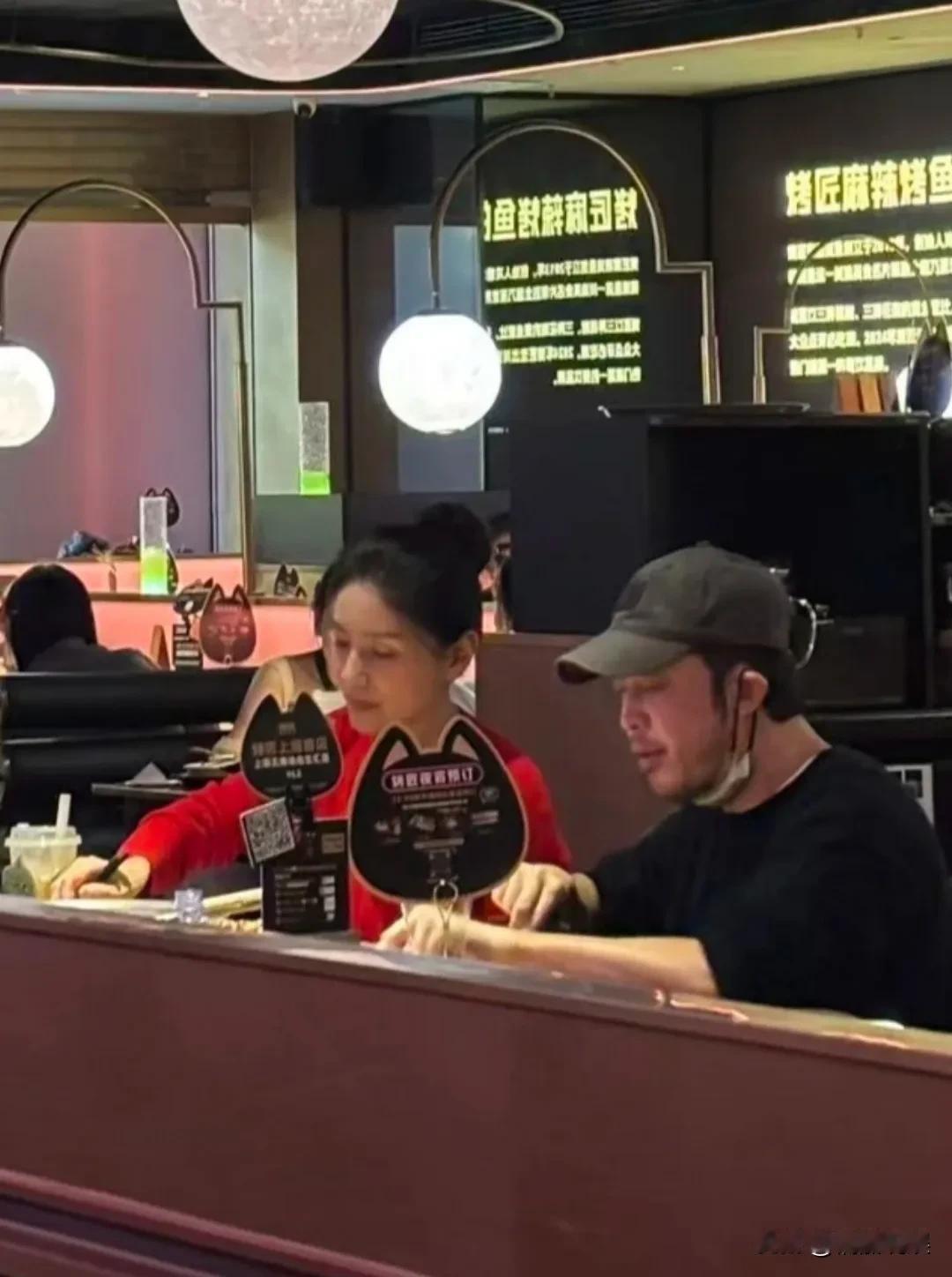 沙溢、胡可两口子一起在餐厅吃夜宵，沙溢戴着棒球帽，穿着一件黑色衣服，感觉有点胡子