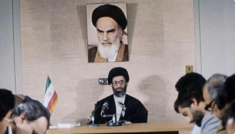 哈梅内伊端坐中央，正在开会。
他身后的墙上挂着霍梅尼的照片。
哈梅内伊（最左边）