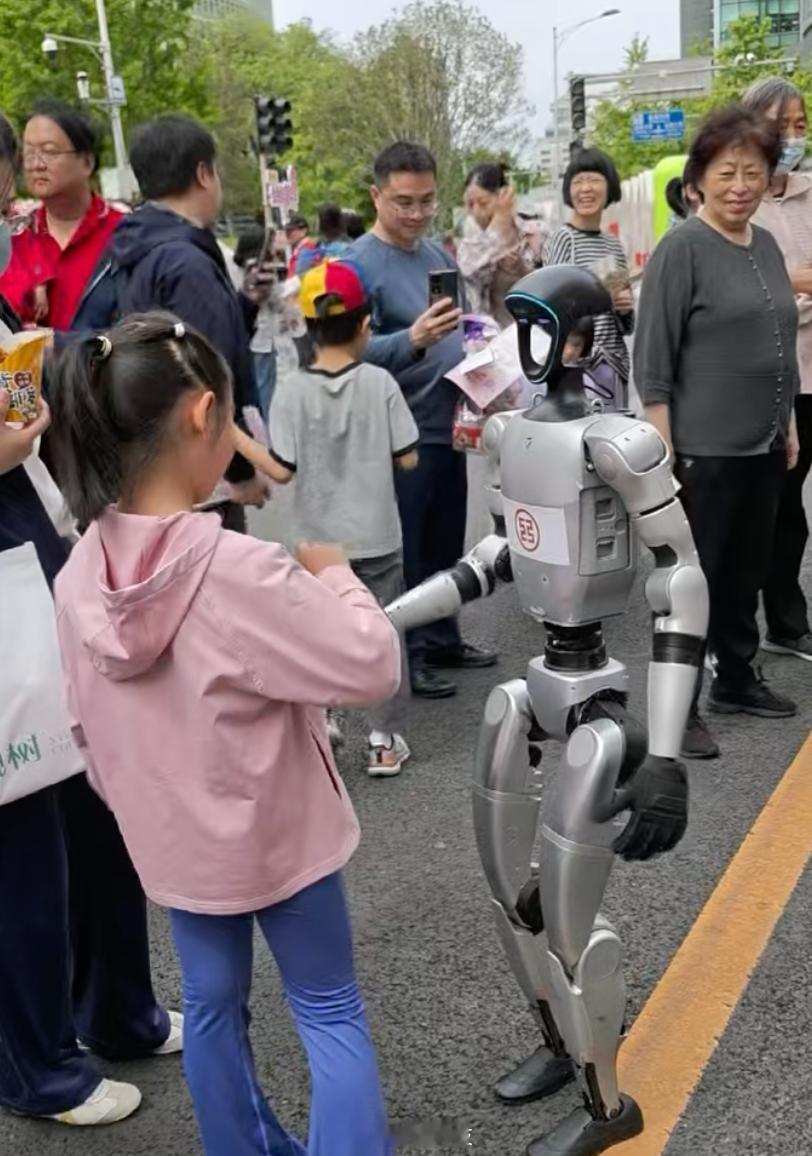 【金融街嘉年华小朋友与机器人握手互动，柴犬见后“走不动”了】4月26日，2026