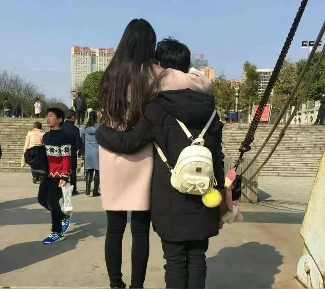 女高男矮，一对情侣，看背影像母子俩。
身高差距大，感觉像是女人在保护男人。