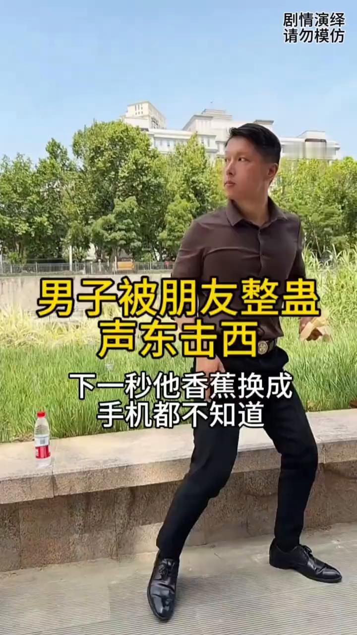 男子被朋友整蛊，声东击西。
男子坐在石板上玩手机，这时旁边的人去拿他的水瓶，谁知