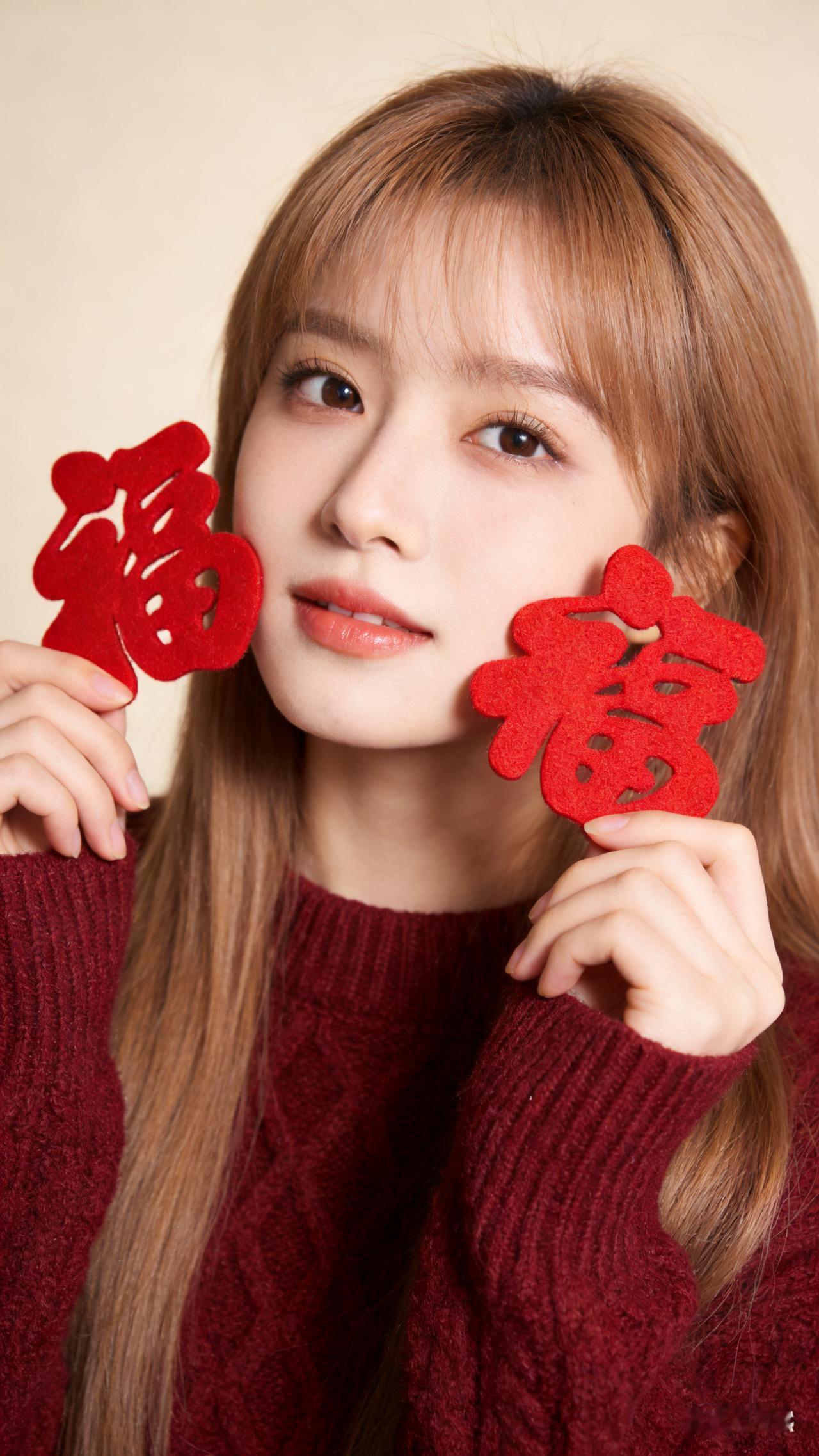 新年写真，少女身着酒红色绞花毛衣，双手各持红毛毡福字轻贴脸颊。浅米色纯色背景，影