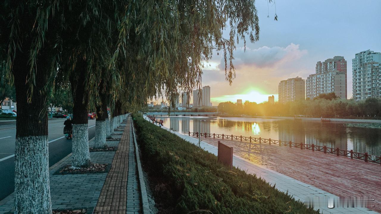 夕阳斜挂，水天一色：夕阳斜挂西山，为天际染上温暖的橘红。平静的河面如明镜，将蓝天