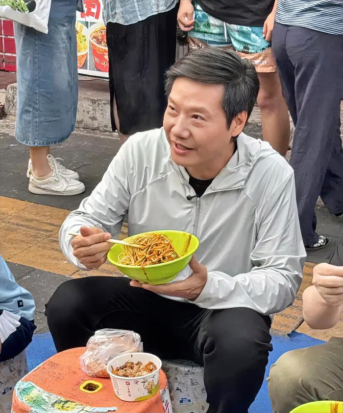 “我靠”！雷军在武汉街头吃早餐这事挺尴尬的。身价千亿的他蹲在马路牙子上，旁边放着