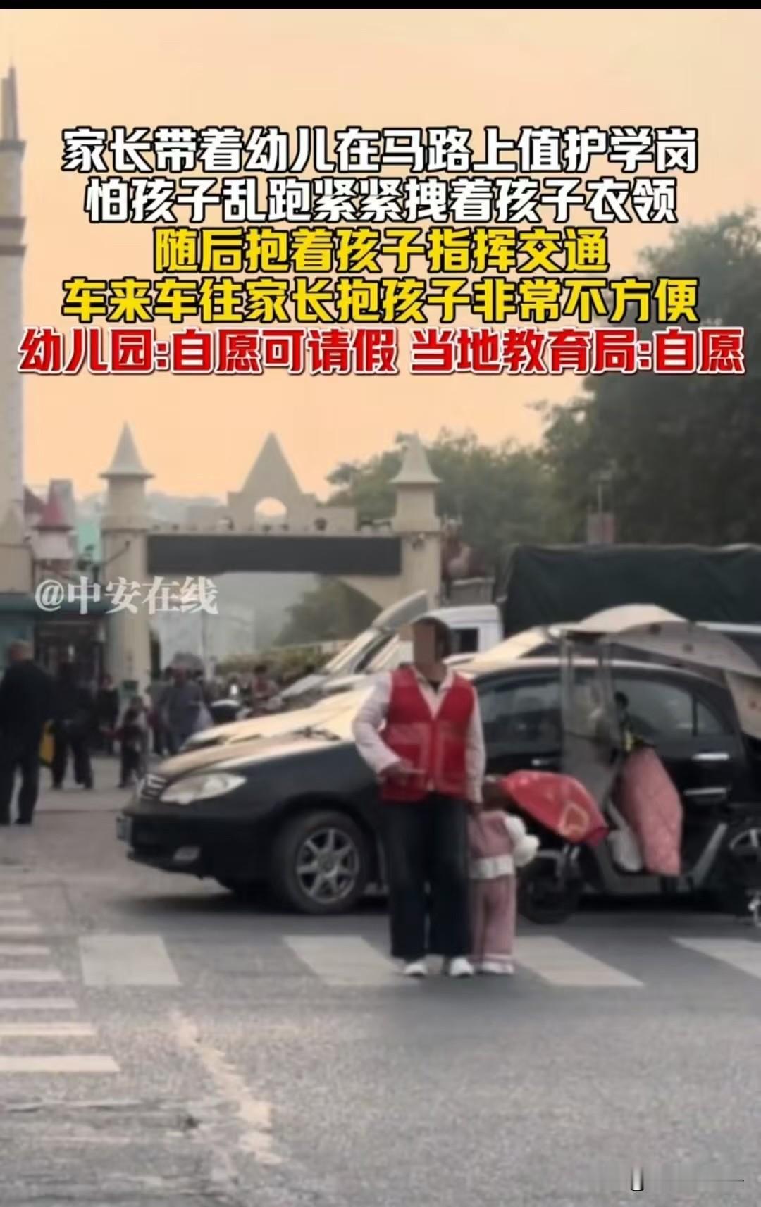 广东，一位家长带着年幼的孩子在车来车往的马路上值护学岗，怕孩子乱跑紧紧拽着孩子衣
