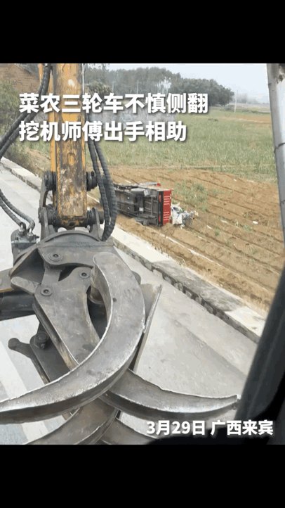 菜农不小心把三轮车翻倒在田里，挖土机师傅恰好路过，马上出手相助，用挖土机把三轮车