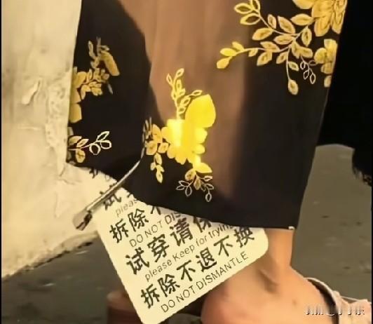 近日，上海一女子穿着黑底金花旗袍，旗袍上挂着一个巨大吊牌，女子逛街拍照1个多小时