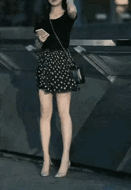 年轻女孩面容精致，秀发披肩，黑色短袖，花式短裙，让人看起来个人气质特别出众，唯独