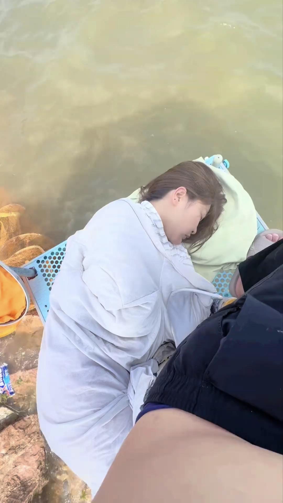 一位姑娘蜷缩着躺在钓台上睡着了，在她身边坐着一位钓鱼人拍下了这美好的一幕。

两