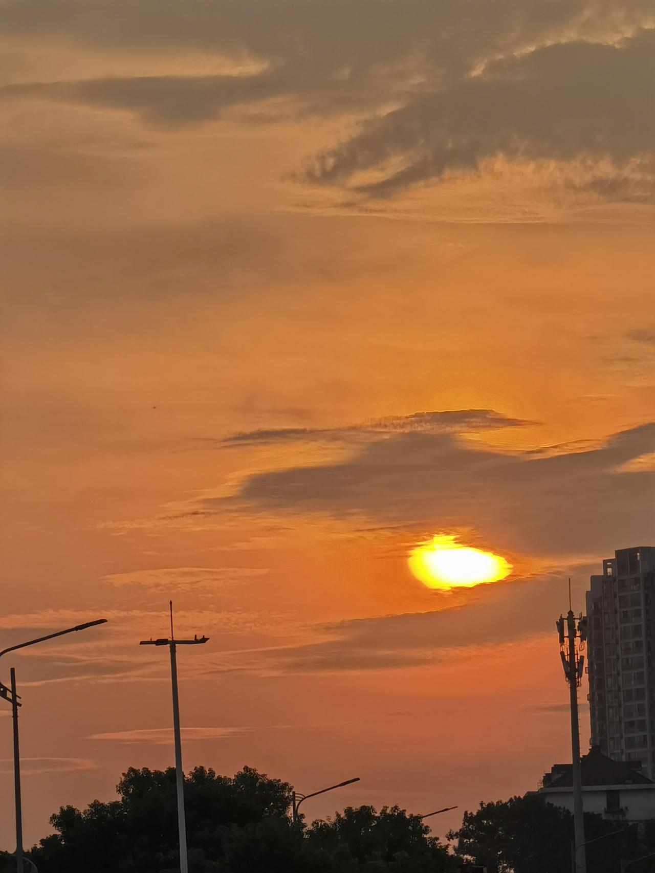 落日漫过城市，晚风捎来一整片橘色温柔。
漫天橘红，楼宇、树影融进温柔暮色。城市的