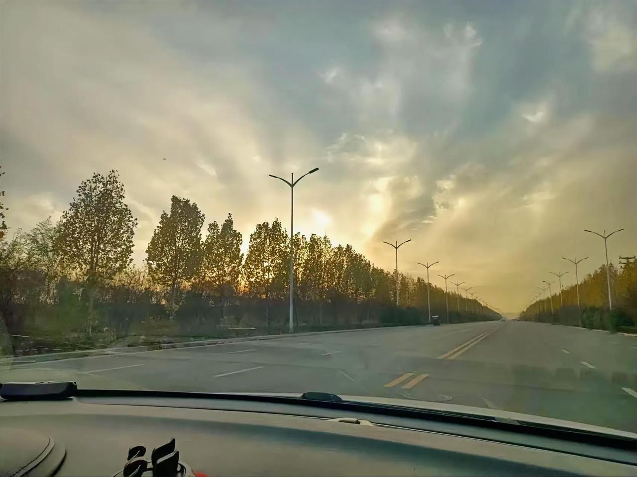 方向盘轻转，窗外的黄昏正给行道树镀上金边。路灯顺着路面铺成两条光带，把空旷的公路