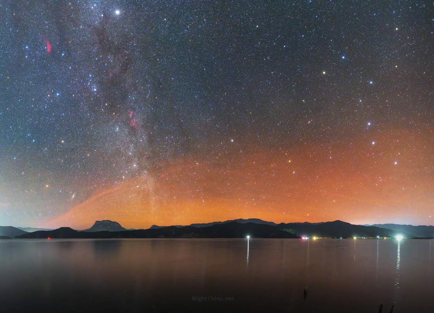 橙色气辉沿着地平线铺陈开来，为夜空增添了一层温暖的底色。银河自天顶垂落，星群清晰