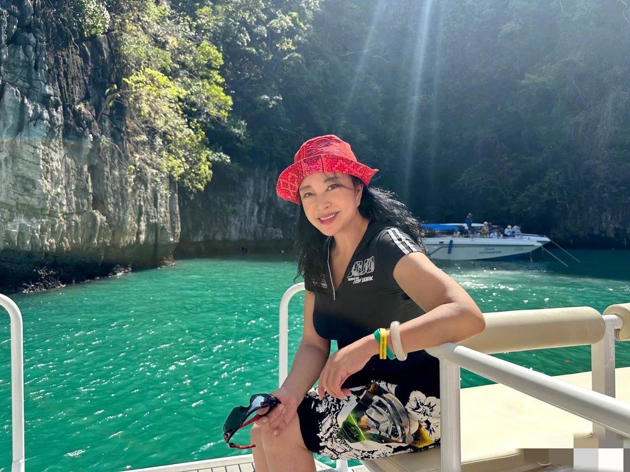 刘晓庆假期旅行照，71岁光彩照人。刘晓庆身穿黑色运动T恤搭配花色短裙，头戴红色帽