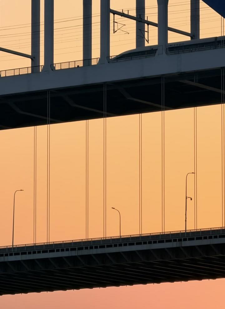 傍晚散步时抬头，就被这双层大桥的剪影撞进了眼里。硬朗的线条在渐变的橘粉晚霞里，像