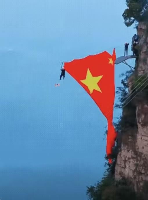 太行山间悬挂巨幅五星红旗工作人员在近乎垂直的红岩绝壁旁，通过高空作业的方式将巨幅