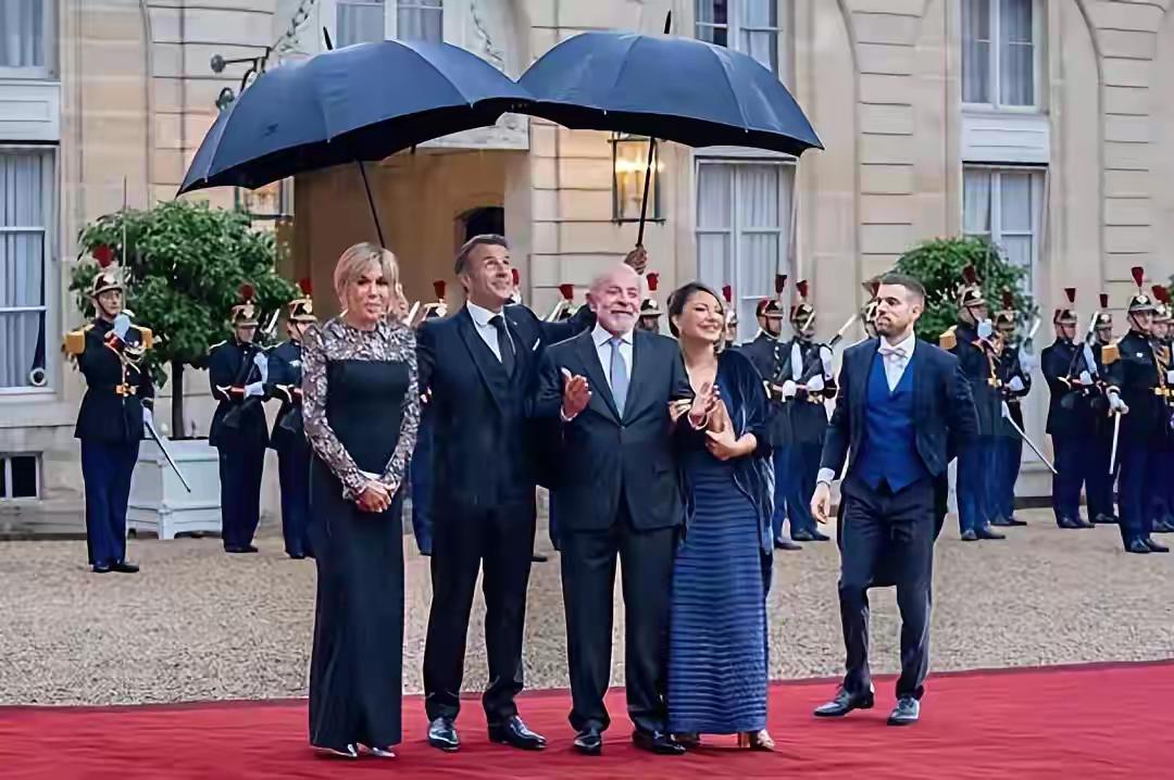 法国总统马克龙亲自为巴西总统夫妇打伞。马克龙夫妇在举行仪式接见来访的巴西总统卢拉