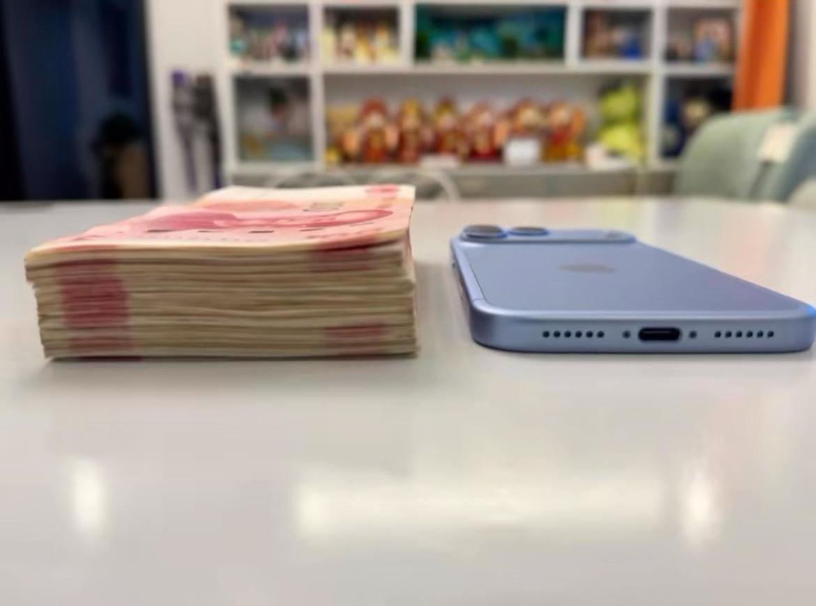 桌上一边是厚厚一沓现金，
一边是iPhone18 Pro Max。
标价1099